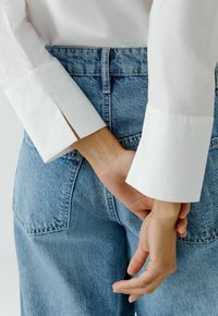 Witte lange mouw shirt met gesplitste manchetten, gecombineerd met hooggetailleerde lichtblauwe spijkerbroek met achterzakken en een gladde textuur.
