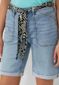 Lichtblauwe denim shorts met een gestreepte zwarte en teal stofriem. Heeft opgerolde manchetten en meerdere zakken. Glad textuur.