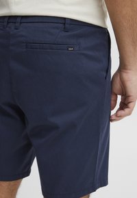 Navy blue shorts made of cotton blend fabric, featuring a back pocket and a small label with the brand name, tailored fit, and smooth texture.