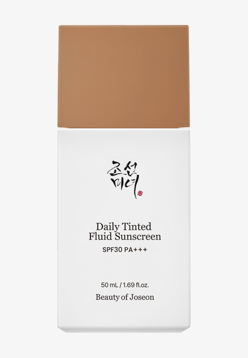 Fluide solaire teinté quotidien, 50 mL. Flacon cylindrique blanc avec un bouchon marron. Texte noir et rouge à l'avant. SPF 30 PA+++