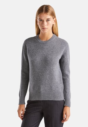 Suéter de lana gris con cuello redondo, dobladillo y puños acanalados, que presenta una textura suave y un corte clásico. Combinado con pantalones a rayas.
