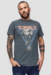 Grijze katoenen t-shirt met een T. Rex-graphic in zwart en rood, blauwe driehoekige omtrek en tekst "1993 TOUR." Korte mouwen, losse pasvorm.