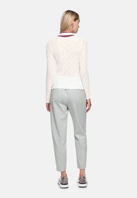 Weiße Langarmbluse mit strukturiertem Muster und abgerundetem Saum, kombiniert mit hellgrauen, zulaufenden Hosen und gemusterten Sneakers.