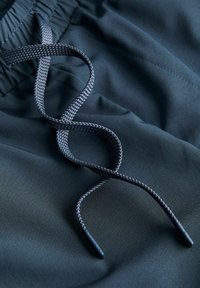 Gros plan sur un tissu bleu foncé avec une ceinture élastique et un cordon tissé noir et gris lâchement bouclé.