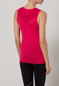 Różowy top sportowy z teksturowanym wykończeniem, bez rękawów, z detalem w kształcie litery V na plecach. Zawiera logo blisko górnej części pleców.