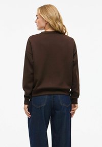 Sweatshirt oversized marron avec un col rond et des manches longues, associé à un jean large bleu, vu de l'arrière.