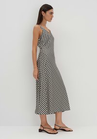 Schwarz-weiß gestreiftes ärmelloses Kleid im Chevron-Muster, knielang, mit V-Ausschnitt und fließender Form. Kombiniert mit minimalistischen schwarzen Sandalen.