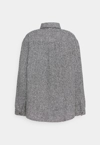 Chemise à manches longues texturée noir et blanc avec un col plié, vue de dos sur un fond clair uni.