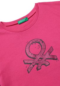 Camiseta de algodón rosa con un diseño de símbolo negro brillante. Cuello redondo con una etiqueta verde "United Colors of Benetton" en el cuello.