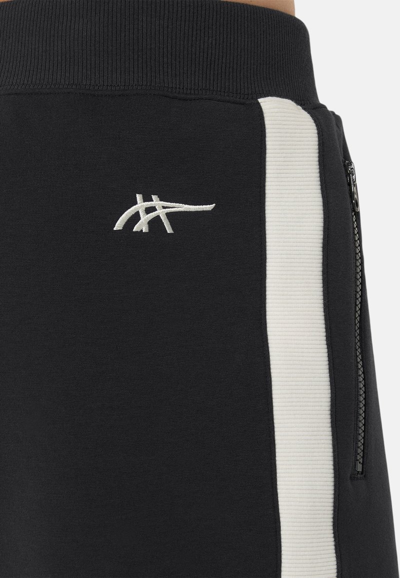 Pantalon de survêtement noir avec une ceinture côtelée, des bandes latérales blanches et une poche zippée argentée. Logo brodé en blanc.