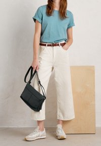 Teal short-sleeve shirt, white wide-leg pants, braided brown belt, black crossbody bag, beige sneakers with textured soles, neutral background.