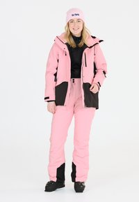Rosa snöjacka med svarta detaljer, matchad med rosa byxor. Har hög krage, dragkedjestängning och logopresent. Strukturerad tyg.