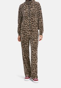 Dres w cętki lamparta z polaru z wysokim kołnierzem i zapięciem na zamek; luźne spodnie; zestawiony z czerwono-białymi sneakersami.