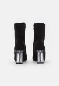 Botines de ante negro con cierre de cremallera, que cuentan con tacones de bloque transparentes. Textura suave y silueta elegante para un diseño moderno.