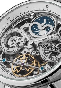 Skeletuurwerk met een zilveren roestvrijstalen kast, blauwe maanfase-display, gouden en zilveren tandwielen, en een dubbele tijd functie.