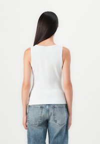 Top alb cu bretele, din material ribbed, cu decolteu rotund, asociat cu blugi din denim de culoare albastru deschis, dotati cu buzunare pe spate si o croiala relaxată.
