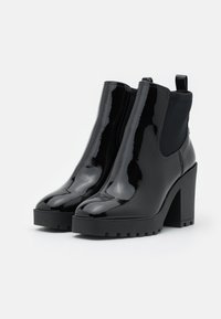 Botas de tobillo de charol negro con un tacón de bloque grueso y una plataforma texturizada. Incluyen paneles laterales elásticos para facilitar su uso.