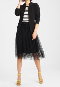 Czarna spódnica z tiulu ozdobiona koralikami, połączona z pasiastym topem i dopasowaną czarną kurtką. Żółte sandały na obcasie dopełniają stylizację.