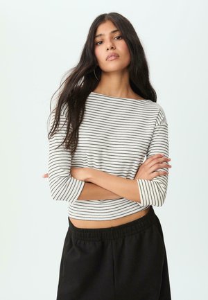 Crop top met horizontale zwart-witte strepen, wijde halslijn en driekwart mouwen. Gecombineerd met zwarte broek met elastische taille.