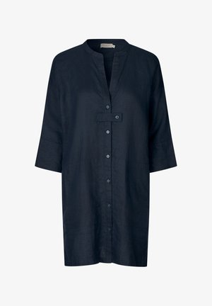 Robe-chemise bleu foncé longueur genou avec manches trois-quarts, col mao, fermeture boutonnée devant et une patte horizontale boutonnée sur la poitrine.