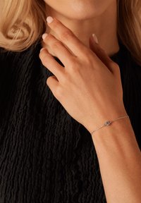 Zilveren schakelpand met een centrale ronde edelsteen, gedragen op een hand tegen een textuur van zwart stof als achtergrond.