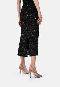Gonna midi nera con paillettes e dettagli con spacco posteriore. Un paio di scarpe con tacco aperto argento dal design elegante e dal tacco sottile.