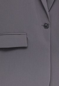 Grau gestreifter Blazer-Stoff mit einem schwarzen Knopf und einer Klappentasche an der Vorderseite.