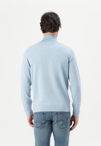 Suéter de punto azul claro con cuello alto y mangas largas. La parte de atrás tiene un dobladillo acanalado y una textura suave y lisa. Combinado con jeans oscuros.
