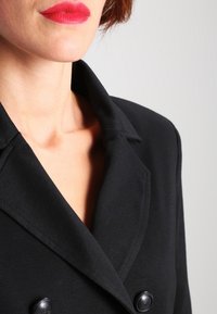 Mustat kaksiriviset bleiseri, jossa on lovellinen kaulus, kaksi mustaa nappia ja sileä pinta, keskittyen yläosan yksityiskohtiin.