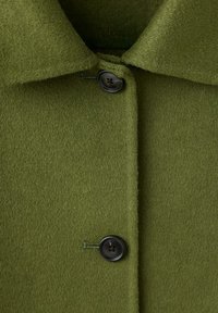 Gros plan d'un manteau en laine vert olive avec deux boutons noirs et un col pointu.