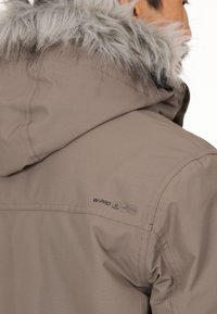 Brun, vandafvisende jakke med en aftagelig hætte, der har en faux fur-kant. Inkluderer W-PRO branding og pleje symboler på skulderen.