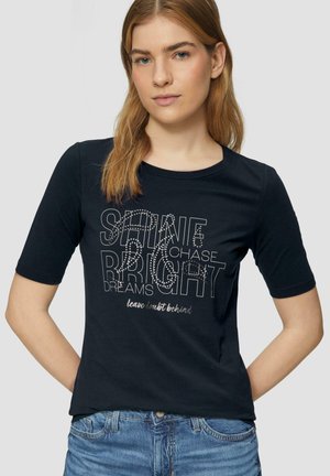 T-shirt noir à manches courtes avec un col rond et une impression sur le devant portant le texte "BRILLE ENCORE POURSUIVANT TES RÊVES" en lettres blanches et argentées.