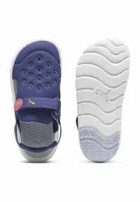 Lilla atletiske sandaler med ventilationshuller, justerbar rem og hvid struktureret sål med et zigzag mønster. Puma-logo detalje.