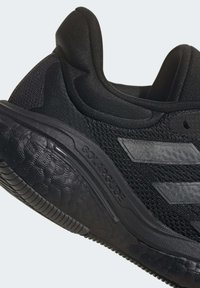 Czarne sportowe sneakersy z teksturowaną siateczką u góry, gładką gumową podeszwą i trzema odblaskowymi paskami. Posiadają wyściełany kołnierz wokół kostki.