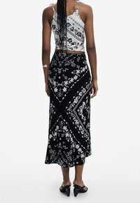 Mustat ja valkoiset kukkakuosiset maksihameet, joissa on liukuhihna, yhdistettynä tiukkaan valkoiseen crop-toppiin, jossa on samankaltainen kuosi.