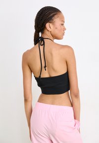 Black halter crop top with ties at the neck, paired with light pink pants. The top is fitted and smooth, exposing the back.