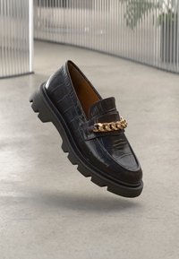 Black patent leather loafer with crocodile pattern, elevated sole, and gold chain accent. Smooth texture, rounded toe design.