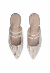 Scarpe slip-on a punta con una base beige, decorate con strass quadrati argentati e due sottili cinturini attraverso il collo del piede.