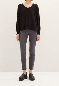Maglietta nera a maniche lunghe con scollo a V, abbinata a pantaloni grigi slim-fit e mocassini neri spessi. Tessuto morbido e silhouette rilassata.