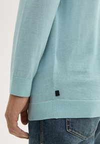 Jasnoniebieski sweter dziergany z długimi rękawami, z prążkowanymi mankietami i dolnym brzegiem, oraz małą czarną metką po boku.