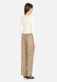 Top lungo a maniche lunghe in maglia bianca a coste abbinato a pantaloni cargo beige. I pantaloni presentano tasche e una vestibilità rilassata, completati da scarpe con tacco nere.