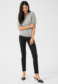 Hall lühikeste varrukatega kampsun valgete triipudega, kokku sobitatud kõrge säärega mustade pükstega ja mustade kontsakingadega, modellil ühevärvilise tausta ees.