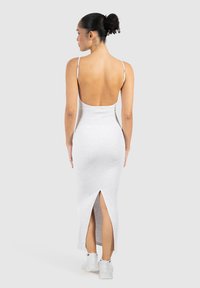 Robe midi gris clair en tissu doux, avec des fines bretelles, un dos nu et une haute fente à l'ourlet. Portée avec des baskets blanches.