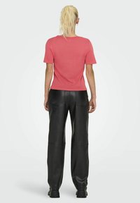 Top de punto rosa con mangas cortas, acompañado de pantalones anchos de cuero negro. El top tiene un escote redondo y una silueta ajustada.