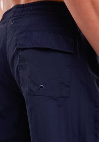 Tamsiai mėlynos šortai, pagaminti iš lengvos medžiagos. Yra galinis kišenė su atvartu ir mygtuku, taip pat laisvas elastinis juosmuo.