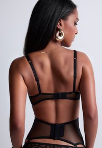 Lingerie noire avec des panneaux en maille transparente, des bretelles réglables et une fermeture à crochet à l'arrière. Caractères avec des détails de bretelles délicates et des accents de dentelle intriqués.