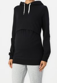 Mustat lyhyt svart hoodie, jossa on pitkät hihat, etupuolella kengurupussi ja nyörit. Yhdistetty vaaleanharmaisiin legginsit värikontrastiksi.