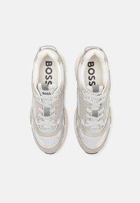 Pár bílých a světle šedých šněrovacích tenisek s polstrovanými límci, síťovinovými panely a potiskem "BOSS" na vložkách a štítcích na jazyku.