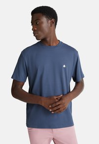 Námořnicky modré bavlněné tričko s krátkými rukávy, kulatým výstřihem a malým bílým logem chobotnice na hrudi. Hladká textura a běžný střih.