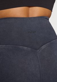 Leggings a vita alta di un blu navy scuro, realizzati in tessuto elasticizzato con una leggera texture mélange e un logo tonale discretamente impresso in rilievo sulla vita.